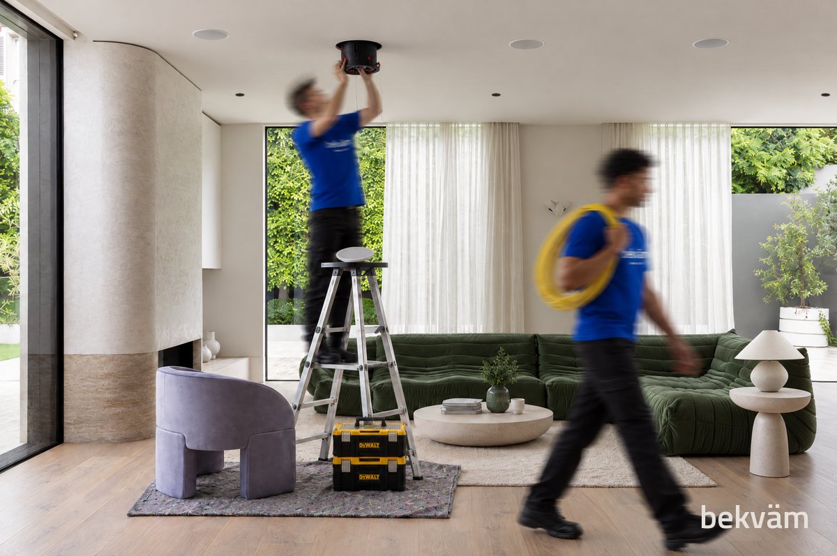 Equipe da Bekväm instalando uma caixa de som no teto de uma sala, com o piso protegido